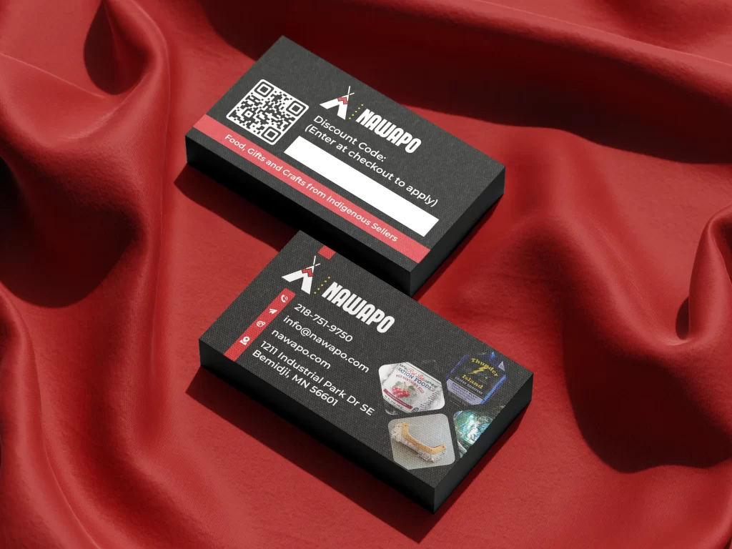 Business card mockup for Nawapo, an indigenous marketplace in Bemidji, MN. The cards feature a high-contrast black textured background with red and white accents. The front includes the brand logo, contact details, a 218 area code phone number, and a four-image grid showcasing featured products like 'Thunder Island' coffee. The back highlights a customer incentive with a QR code and a blank white field for a custom checkout discount code.